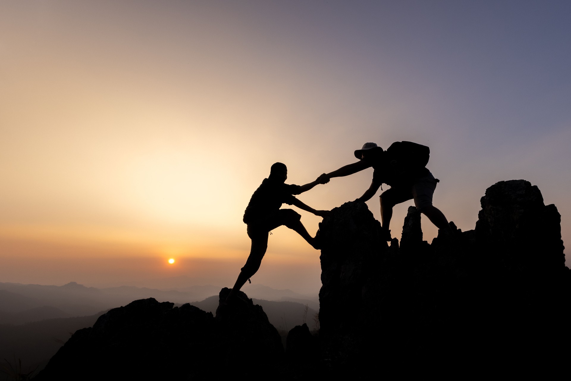 Silhouette de randonneurs grimpant sur une falaise de montagne et l’un d’eux donnant un coup de main. Les gens aident et, concept de travail d’équipe.