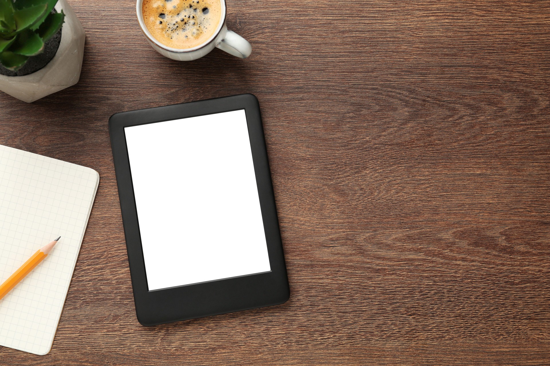 Lecteur d’ebook moderne, plante, café et cahier sur table en bois, pose plate. Espace pour le texte